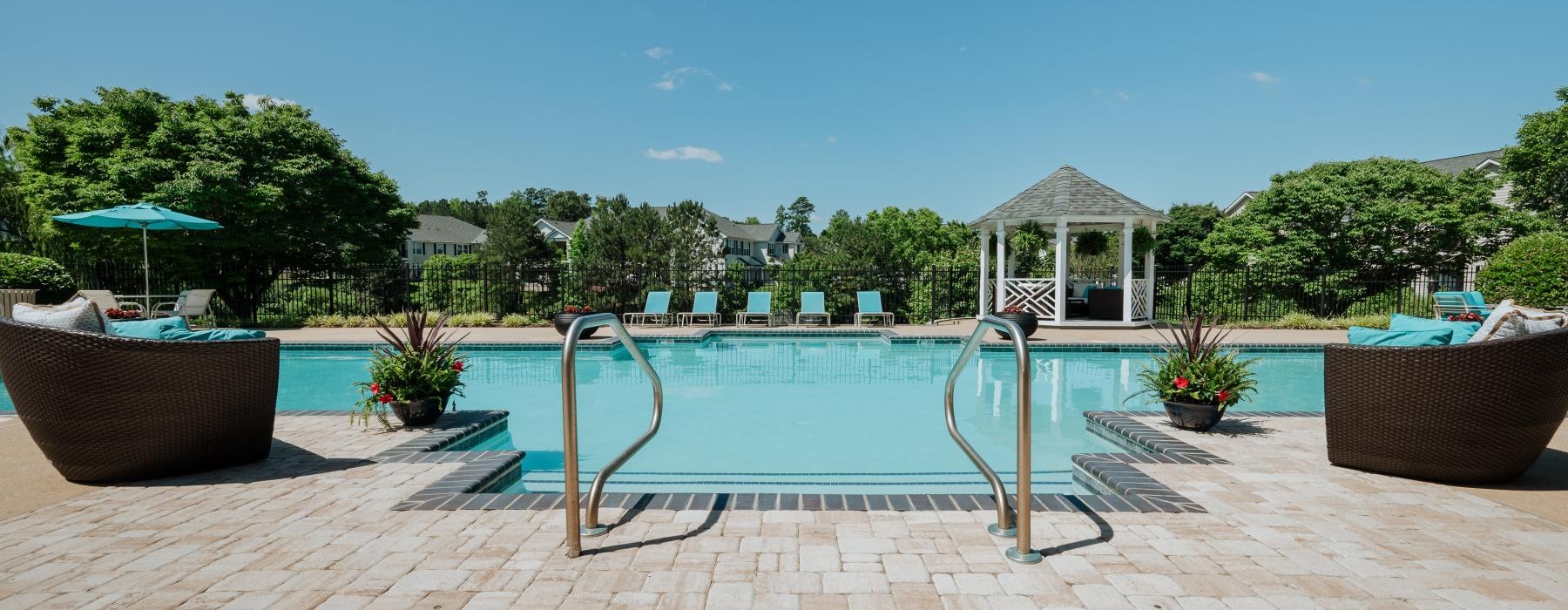 a pool with a deck and chairs by it and trees in the back